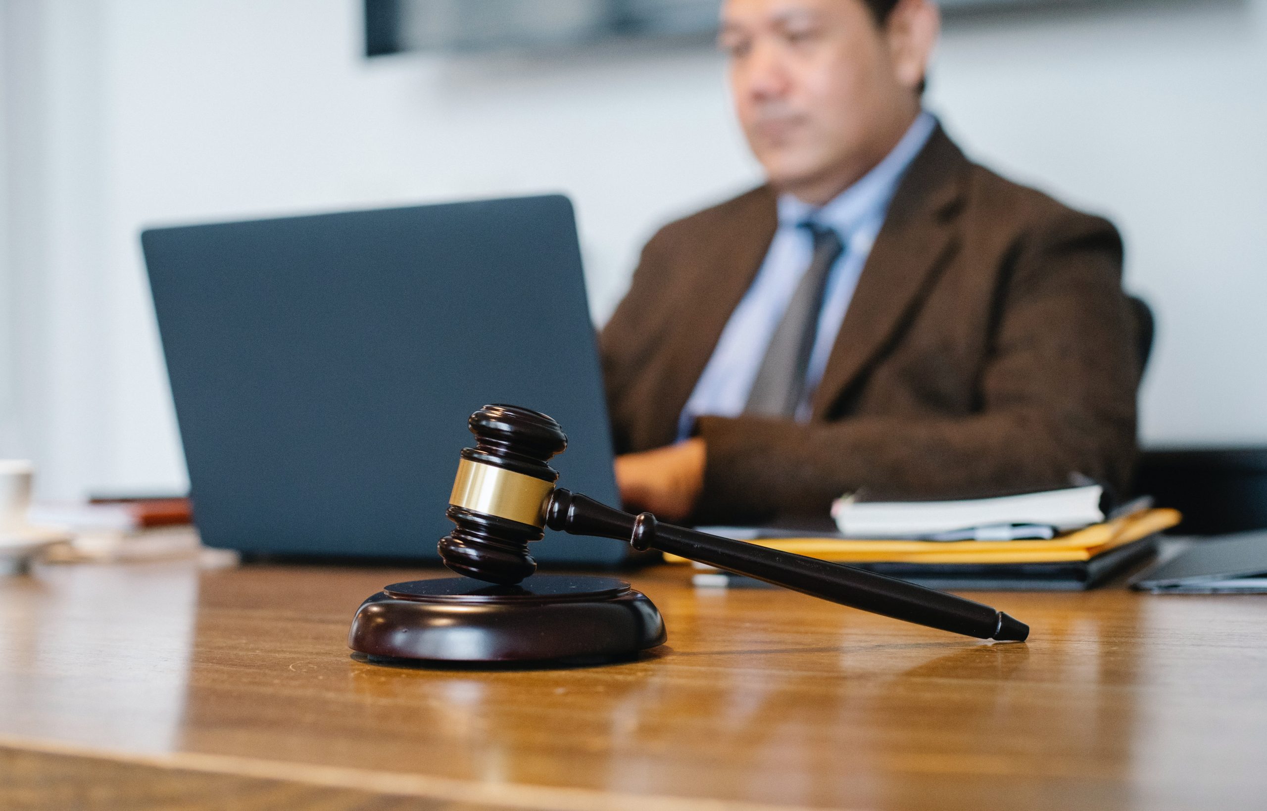 Blurred focus photo of a gavel in front of a plain-clothes judge working on a laptop computer