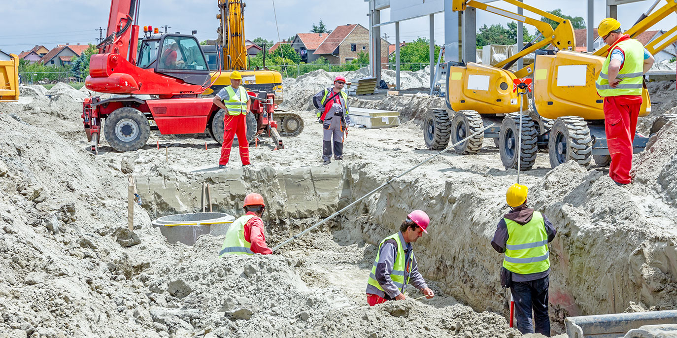 Several workers dig a pit at a construction site while supervisors watch from above.