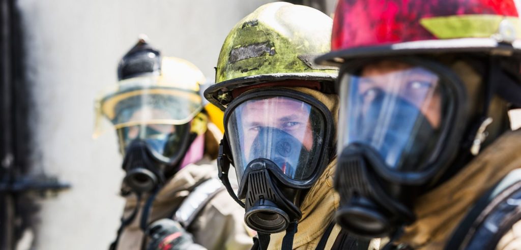 Three firefighters prepared to do their jobs look directly at the camera.