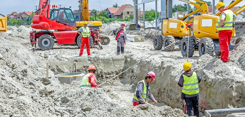 Several workers dig a pit at a construction site while supervisors watch from above.