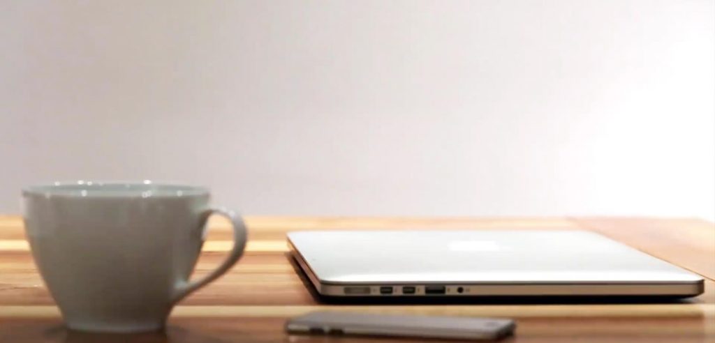 A laptop, phone, and cup rest on a wooden table.