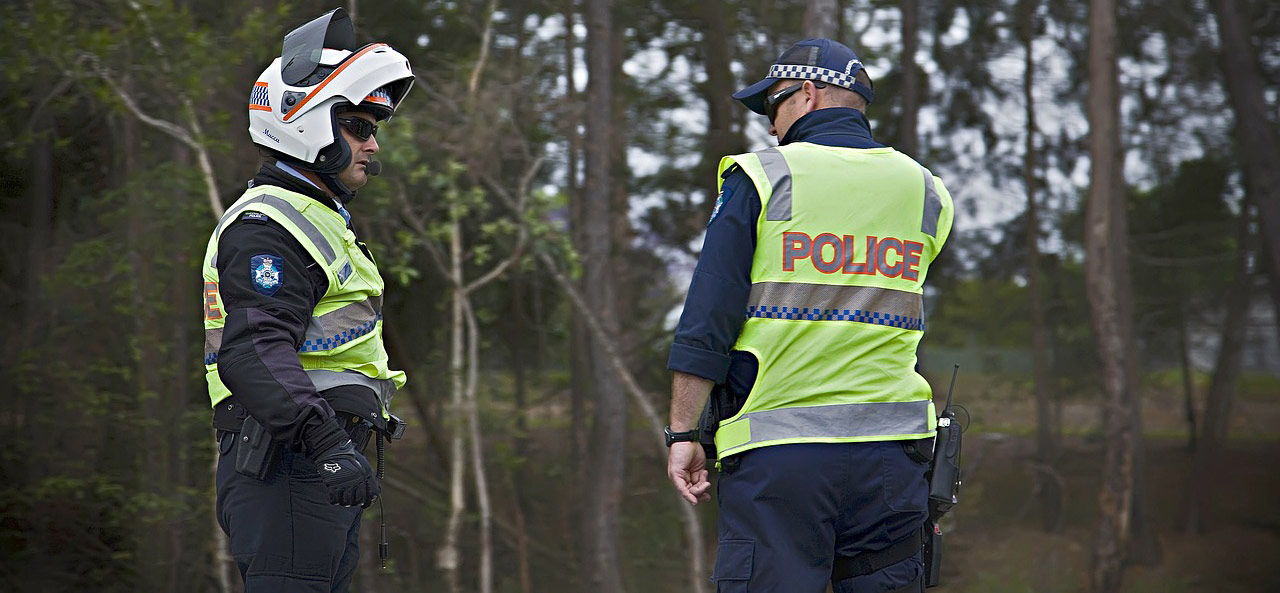 Two police officers speak to each other outdoors on the scene of an incident.