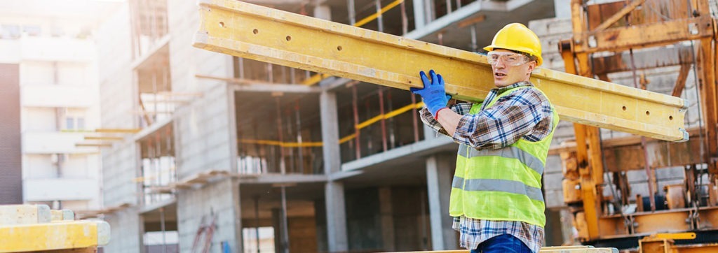 A worker holding a girder catches his breath while looking at the camera.