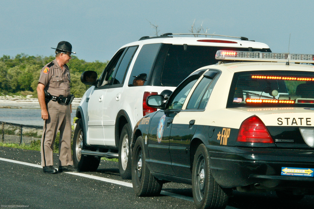 A state trooper addresses a driver he has detained on the shoulder of a roadway.