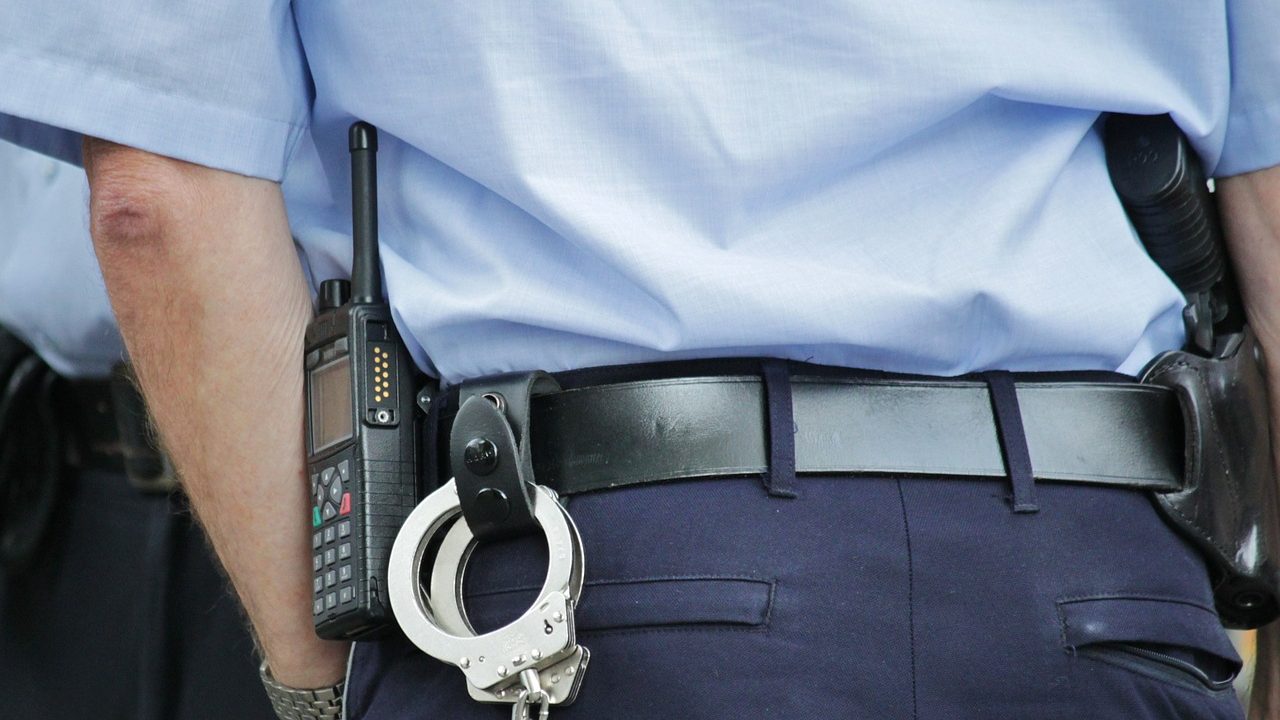 A police officer and his duty belt holding a radio, handcuffs, and a holster and pistol.