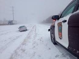A state trooper stops to assist a silver sedan that has gone off the road during inclement winter weather.